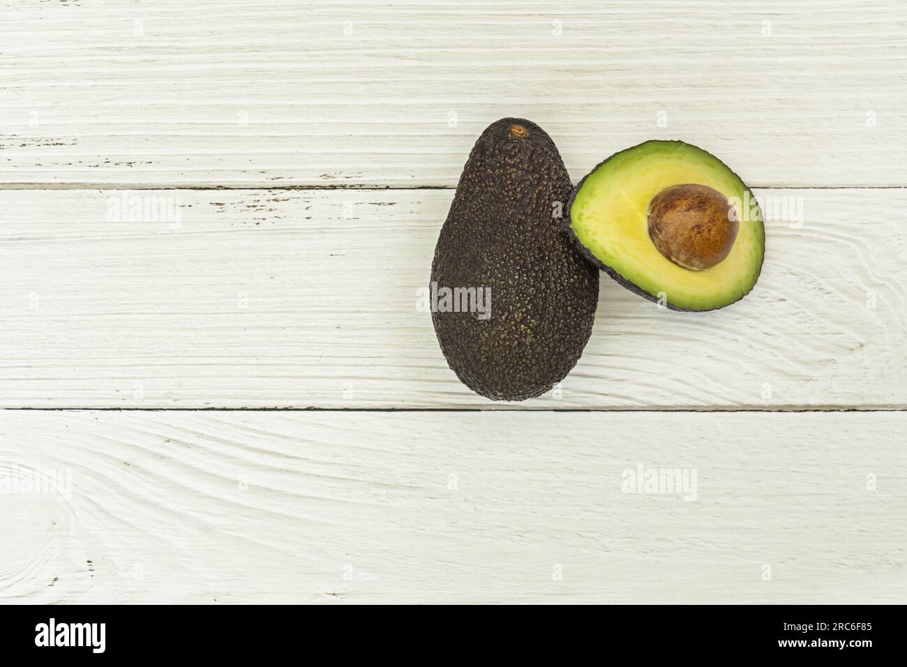 Un avocado maturo e un altro tagliato a metà con il suo grosso seme su un tavolo di legno bianco Foto Stock