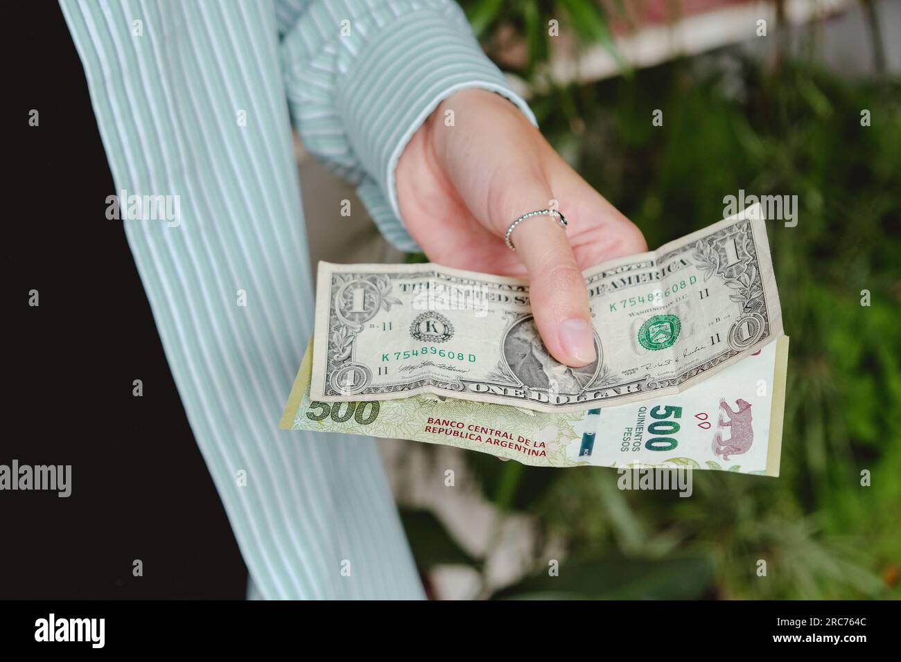 Donna che tiene pesos argentini e una banconota da un dollaro. Aumento del dollaro in Argentina.1 dollaro è pari a 500 pesos argentini. Foto Stock