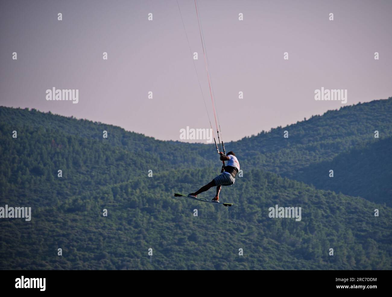 Kite surfer in azione mentre salta con la costa sullo sfondo Foto Stock