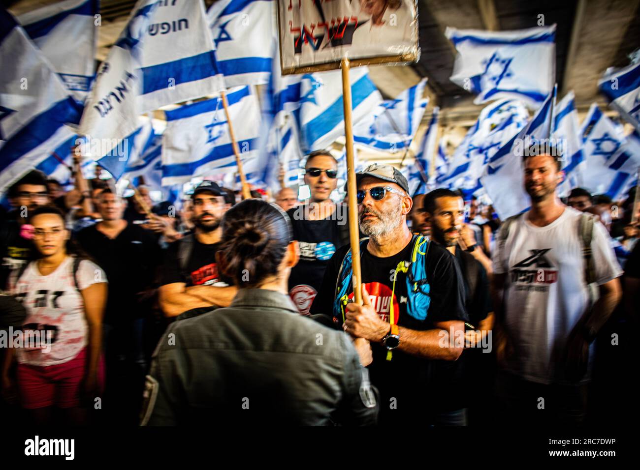 Un manifestante tiene un cartello mentre altri sventolano bandiere israeliane durante una manifestazione all'aeroporto internazionale Ben Gurion. La polizia israeliana si è scontrata con i manifestanti in mezzo a enormi manifestazioni contro i controversi piani di riforma giudiziaria del governo. Le proteste sono scoppiate dopo che un disegno di legge per rimuovere il potere della Corte Suprema di rivedere le decisioni dei ministri ha approvato la sua prima lettura in parlamento lunedì sera. Le riforme hanno polarizzato il paese, scatenando mesi di manifestazioni di massa. (Foto di Eyal Warshavsky/SOPA Images/Sipa USA) Foto Stock