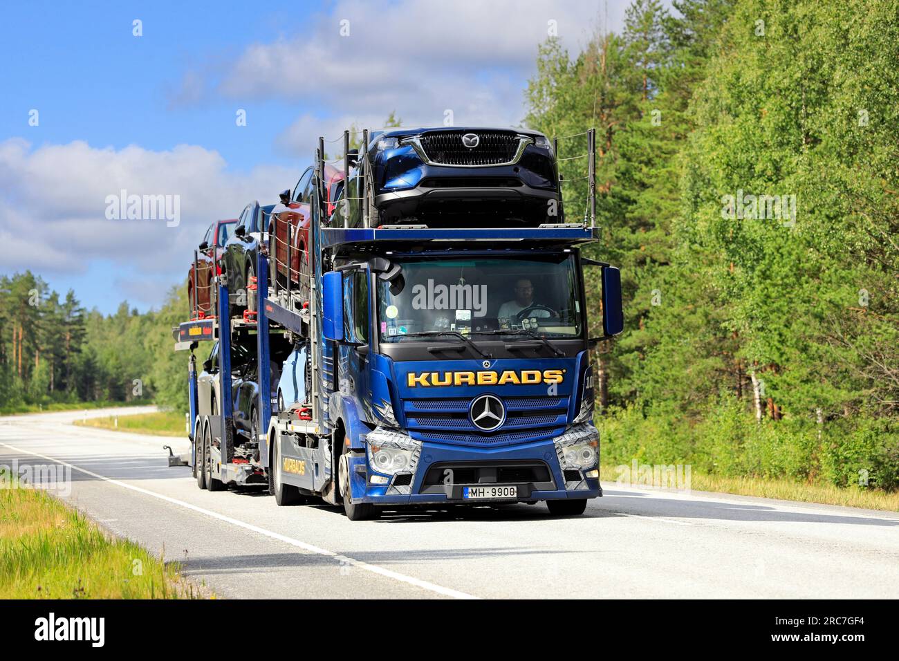 Il camion blu Mercedes-Benz Actros di Kurbads trasporta nuove auto lungo la strada 25 in un giorno d'estate. Raasepori, Finlandia. 7 luglio 2023 Foto Stock