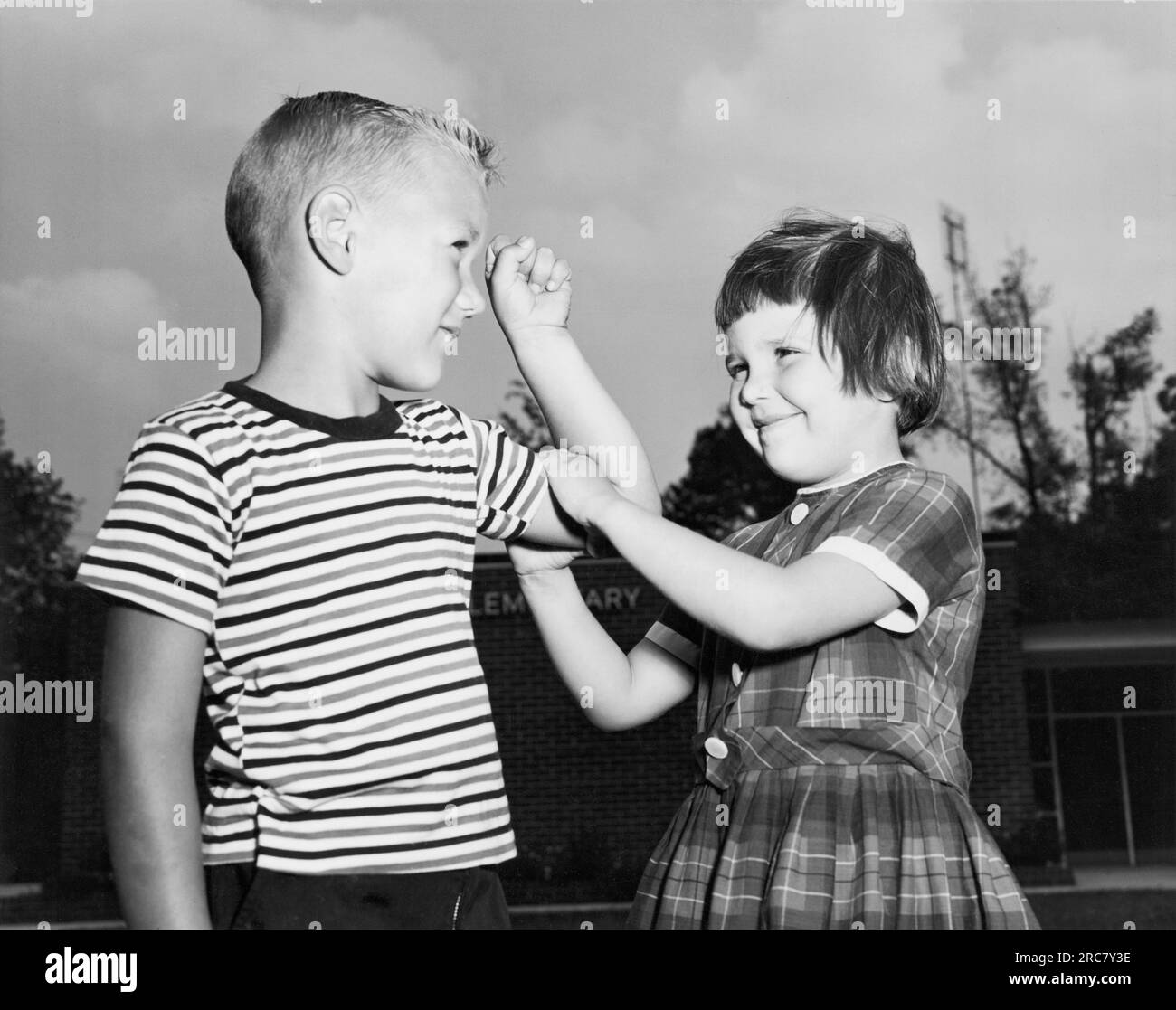 Maryland: 1965 Una giovane ragazza sente il muscolo bicipite di un giovane ragazzo. Sono in asilo ed entrambi sono partecipanti al National School Lunch Program amministrato dagli Stati Uniti Deaprtment of Agriculture. Foto Stock