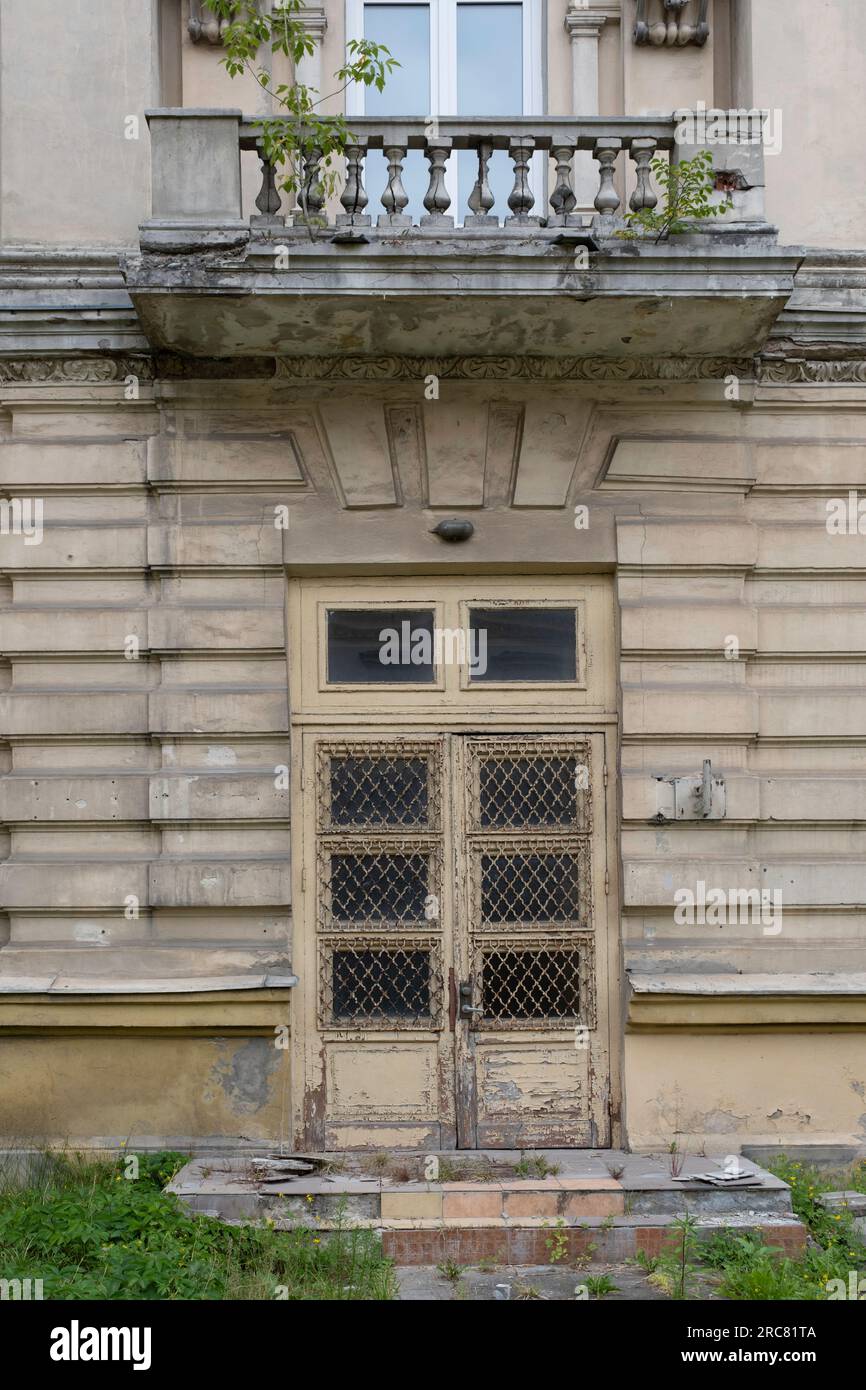 Vecchia porta in una casa abbandonata inabitabile con rete davanti alle finestre in un muro di pietra intemprato con un balcone sopra di essa a Vilnius, in Lituania Foto Stock