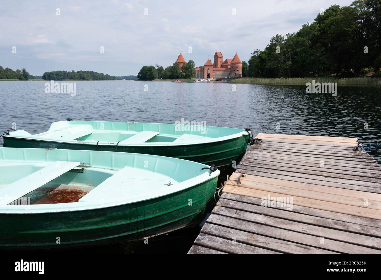 Molo di legno con barche turistiche sul Lago Galve, sullo sfondo il Castello di Trakai, costruito nel XIV secolo e servito come residenza per i Granduchi Foto Stock