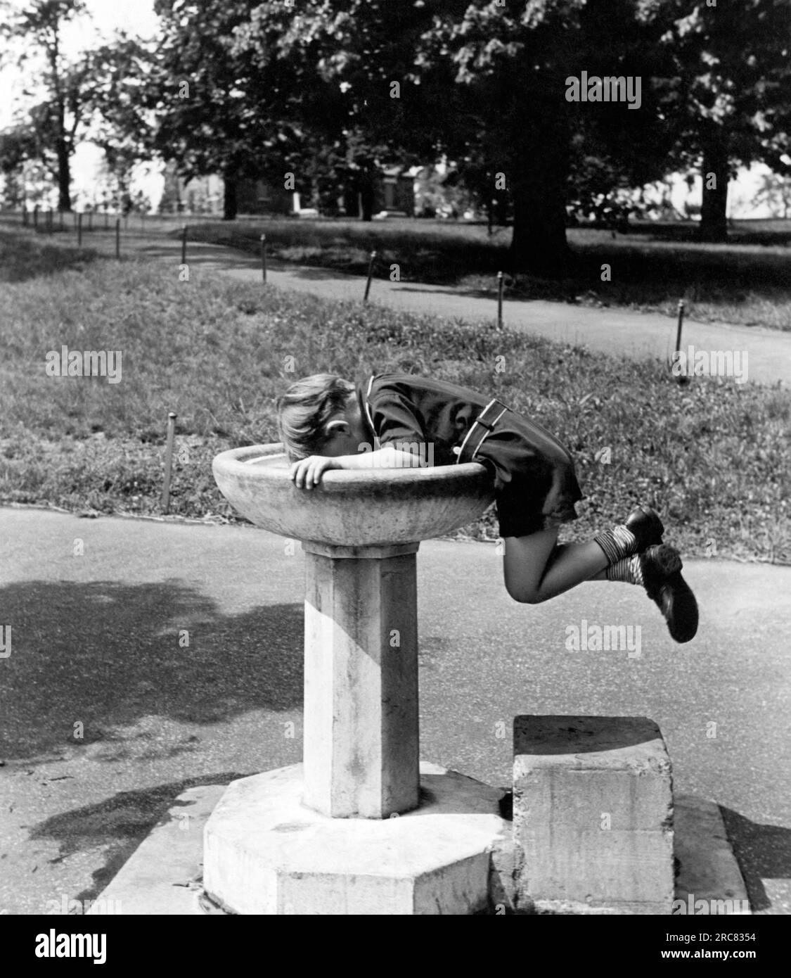 Stati Uniti: c. 1932 Un giovane intraprendente prende un drink d'acqua da una fontana. Foto Stock