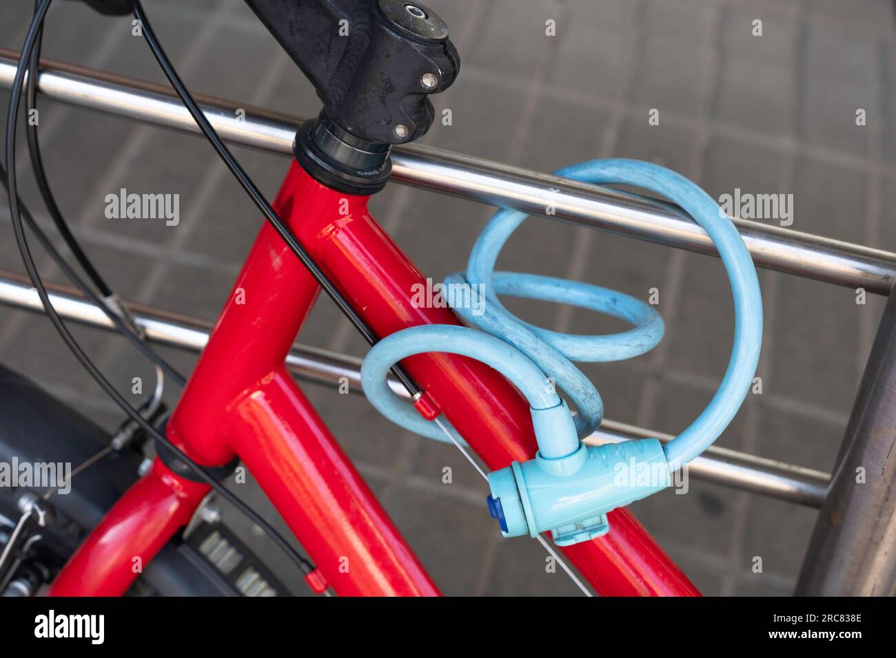 La bicicletta rossa è fissata saldamente a un tubo in acciaio inox con un blocco cavo blu per bicicletta. Dettagli Foto Stock