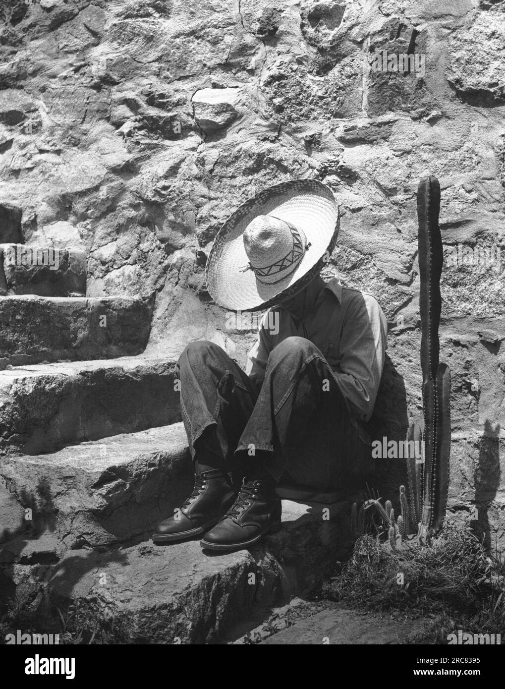 c. 1950 Un uomo che indossa un sombrero fa una siesta sui gradini accanto a un cactus. Foto Stock