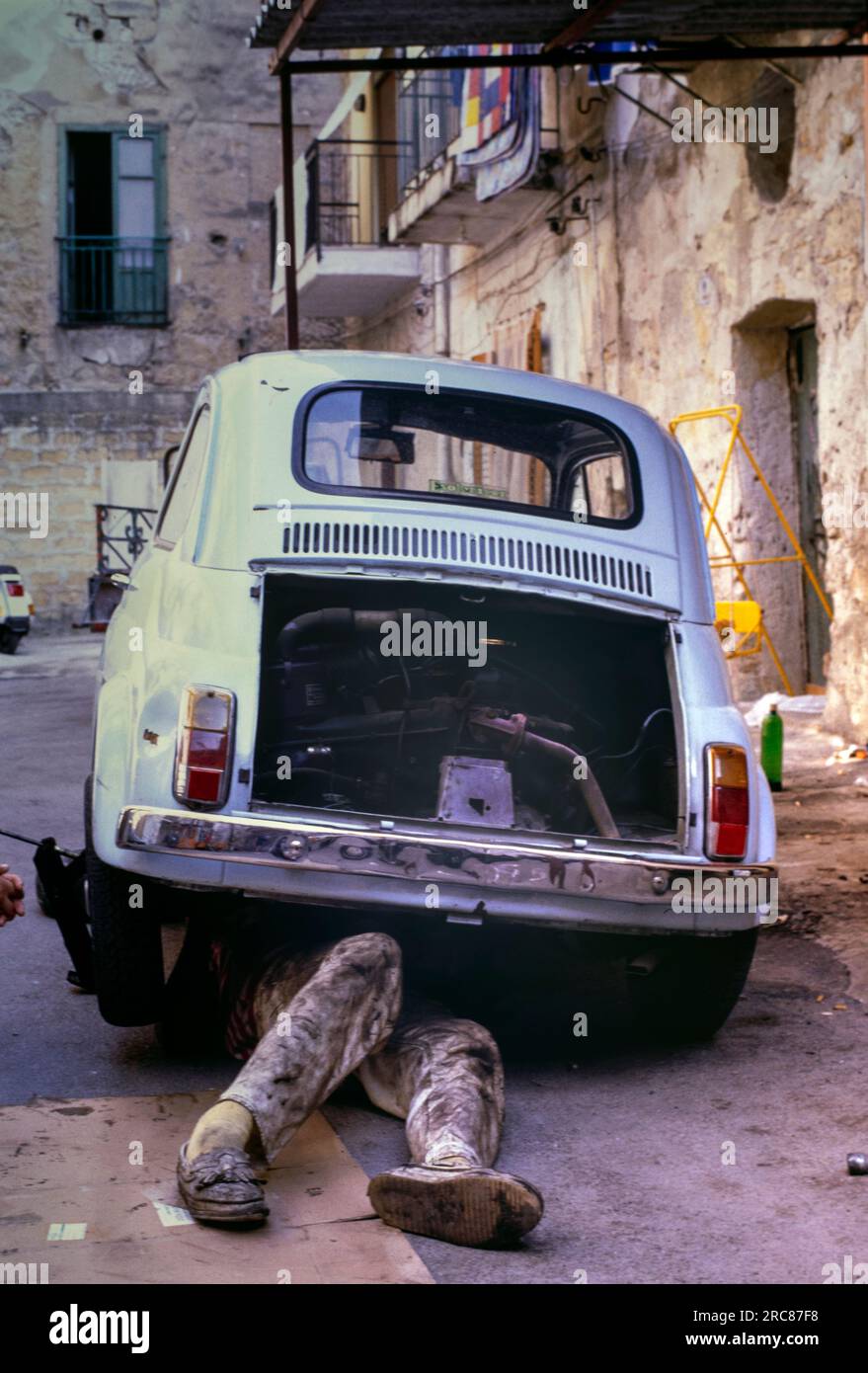 Uomo che lavora sotto una vecchia Fiat 500, Palermo, Sicilia. Foto Stock