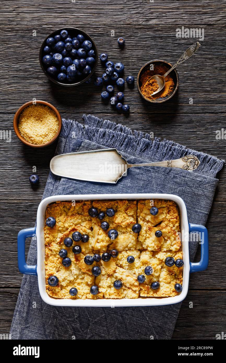 Crumble di mele fatto in casa con mele, cannella, spezie, crumble dolce e burroso e mirtilli freschi cosparsi sopra in un piatto da forno su legno scuro Foto Stock