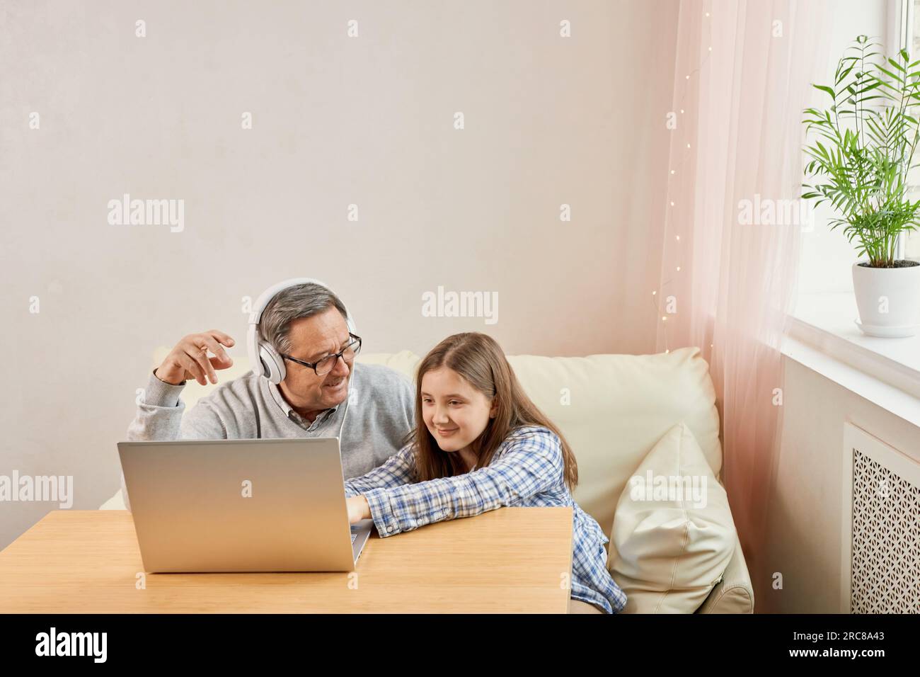 Nipote che aiuta il nonno a fare comunicazioni on line su un laptop, ascoltando musica moderna, vecchio con sua nipote che usa il computer portatile V Foto Stock