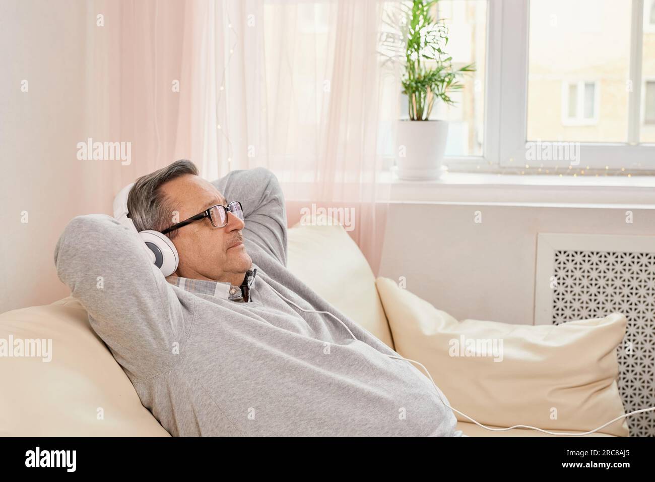 Uomo anziano con le cuffie mentre ascolta la musica. Senior riposa in un ambiente confortevole per il tempo libero, godendo della serenità di un invecchiamento sano e.. Foto Stock