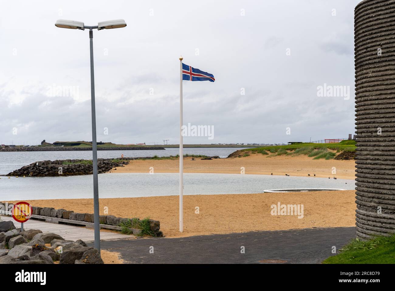 Sventolando la bandiera islandese nella deserta spiaggia di Nautholsvik a Reykjavik, Islanda Foto Stock