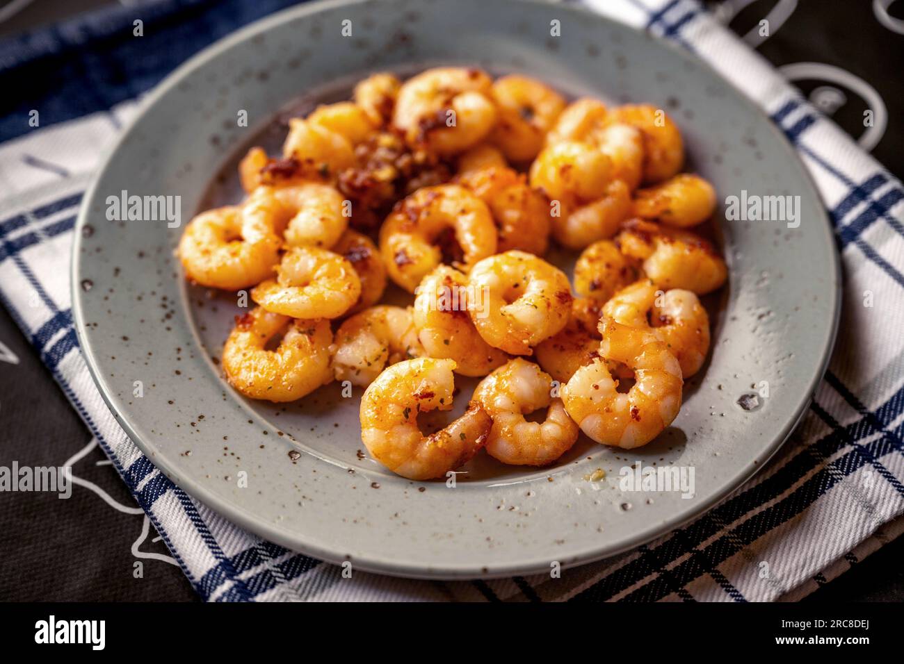 Gamberi grigliati con peperoncino in piatto grigio su un asciugamano sul tavolo, primo piano. Foto Stock