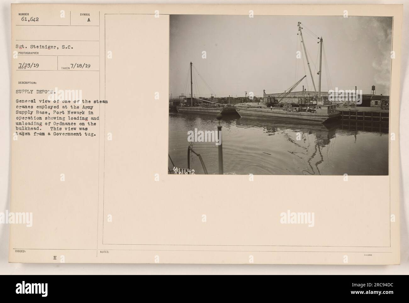 Una gru a vapore è vista presso la base di rifornimento dell'esercito a Port Newark, impegnata nel carico e nello scarico di ordigni sulla paratia. La foto è stata scattata dal sergente Steiniger il 18 luglio 1919, da un rimorchiatore governativo. Questa è una visione generale di uno dei depositi di rifornimento che mostra attività militari durante la prima guerra mondiale. Foto Stock