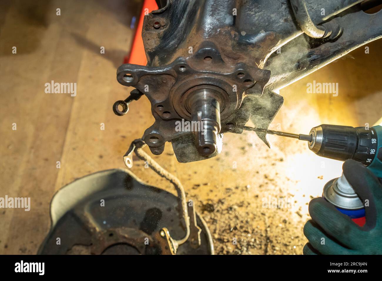 Il meccanico della vettura esegue una filettatura sul cuscinetto del mozzo della ruota posteriore e spruzza l'olio per raffreddarlo. Manutenzione automatica. Riparazione. Officina. Foto Stock