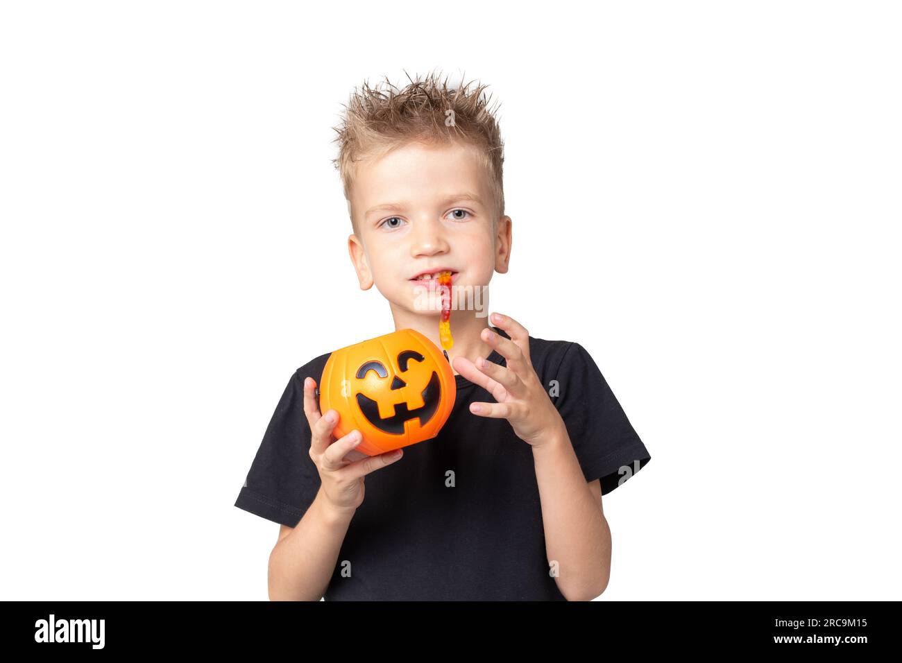 Bambino di Halloween con secchielli di zucca che mangia caramelle su uno sfondo bianco dello studio. Un ragazzo felice che tiene in mano il cestino Jack-o-Pumpkin per raccogliere il trucco delle caramelle o. Foto Stock