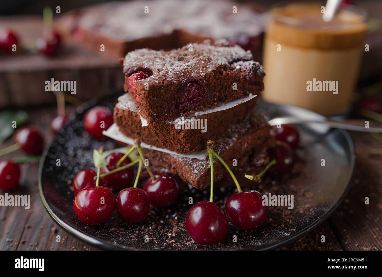 Torta al cioccolato con ciliegie su un piatto nero su un tavolo di legno Foto Stock