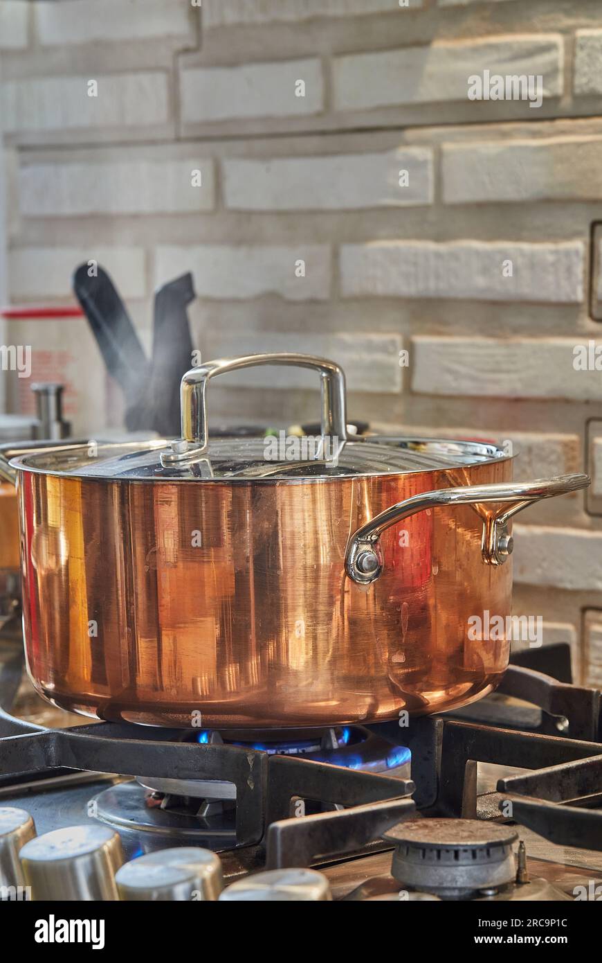 La pentola in rame con coperchio e piatto viene cotta sul fuoco sulla stufa  a gas. Il vapore sale sopra la pentola Foto stock - Alamy