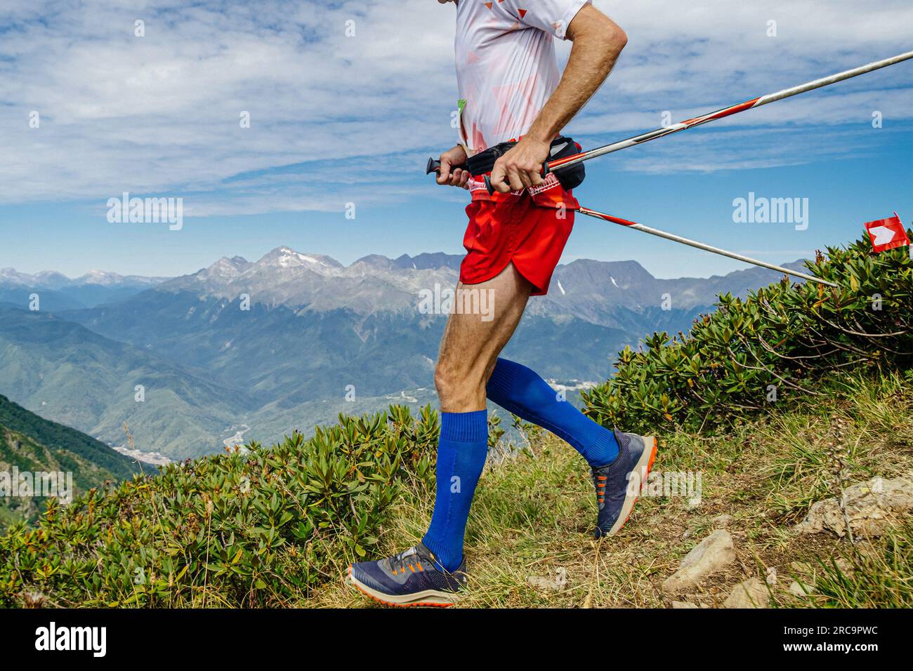atleta maschile che corre dal lato della montagna con calze a compressione ai piedi e bastoncini da trekking in mano Foto Stock