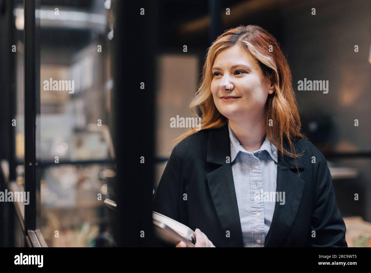 Donna d'affari sorridente che guarda via mentre si trova in ufficio Foto Stock