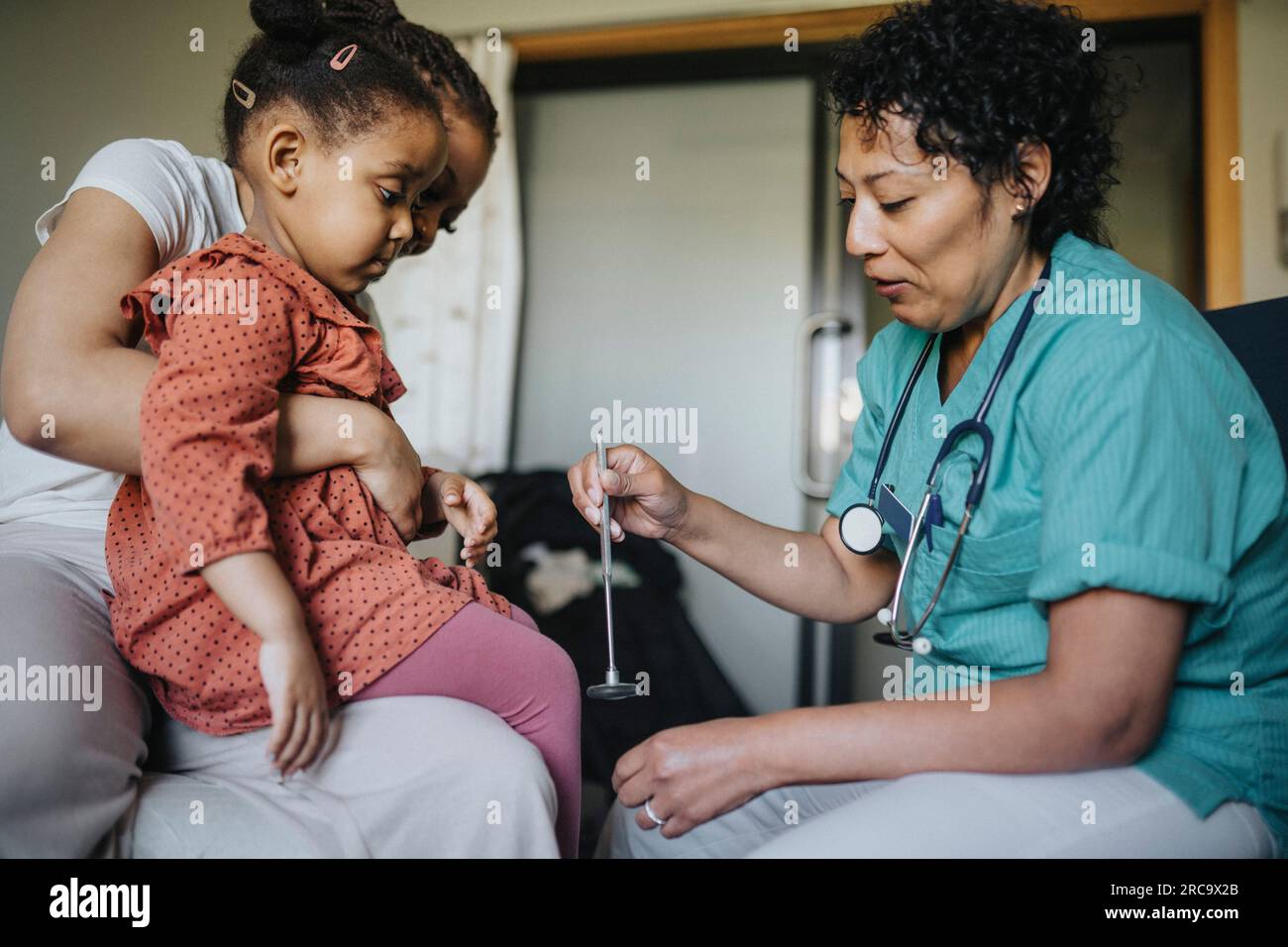 Medico donna con martello riflettente che esamina la ragazza in clinica Foto Stock