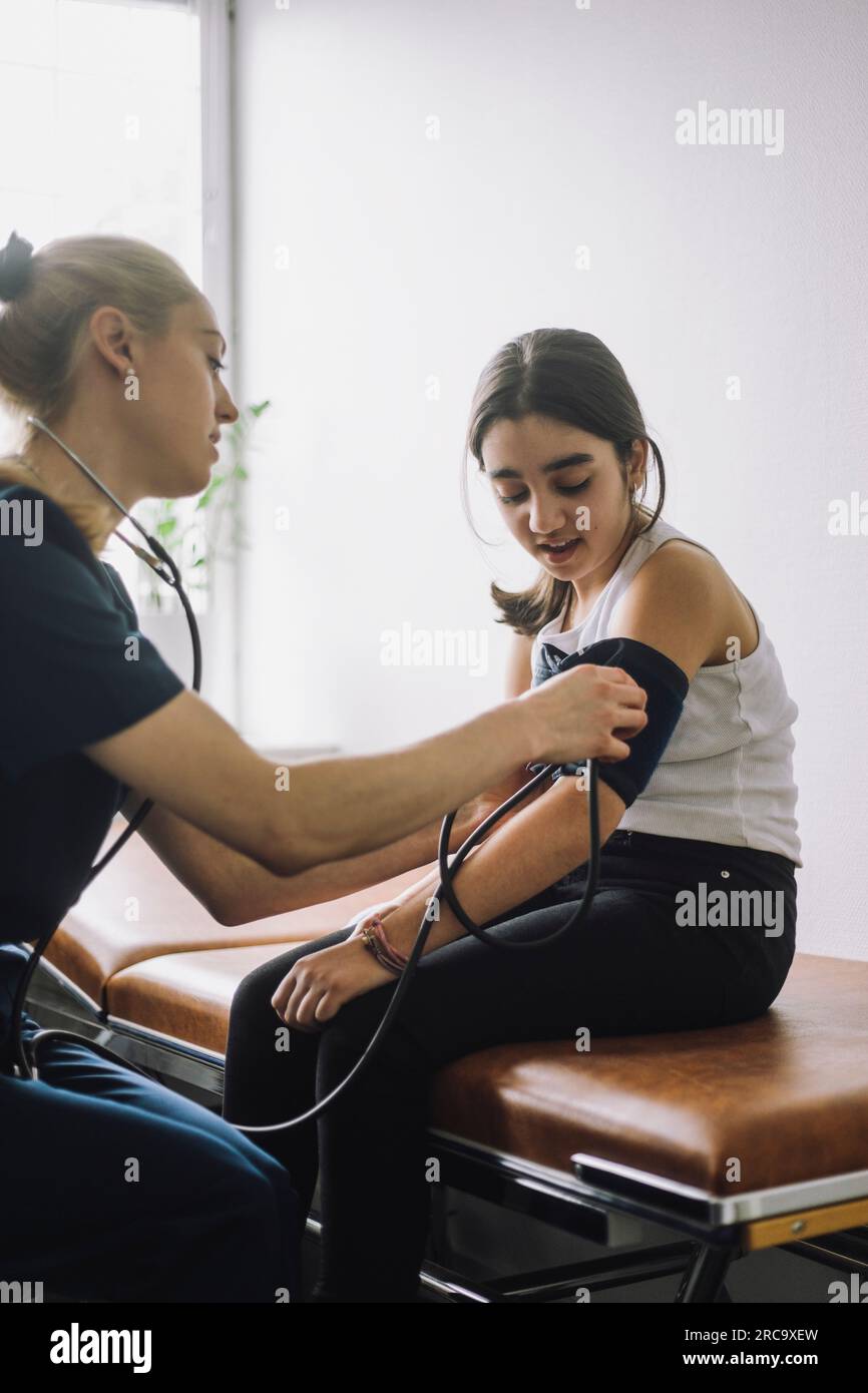 Infermiera donna che controlla la pressione sanguigna di una ragazza seduta sul letto in clinica Foto Stock