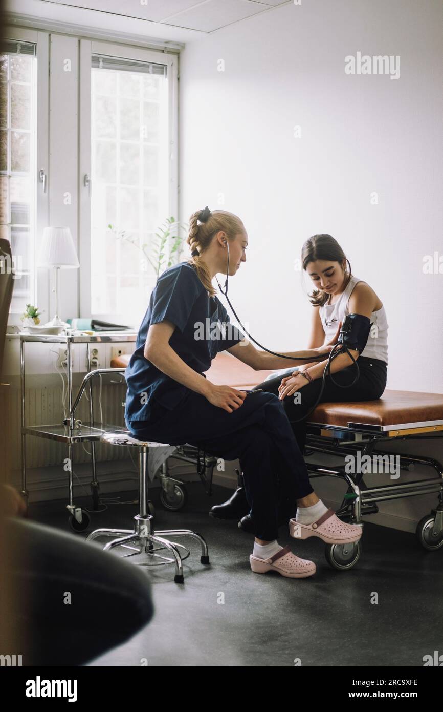 Infermiera donna che esamina la pressione sanguigna di una ragazza seduta a letto in clinica Foto Stock
