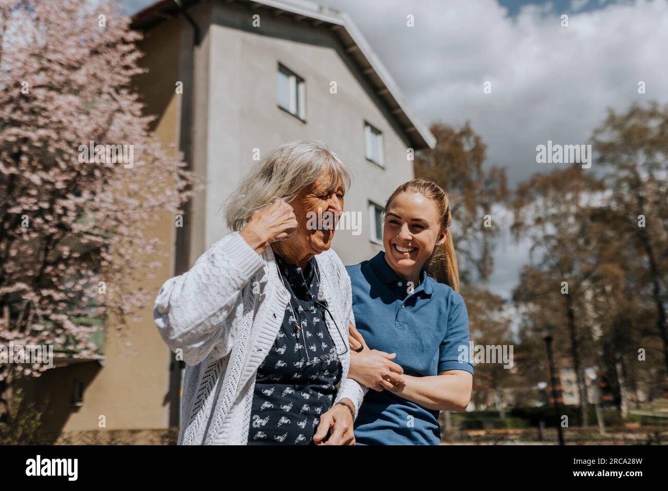 Infermiera donna felice con braccio a braccio di donna anziana durante la giornata di sole Foto Stock
