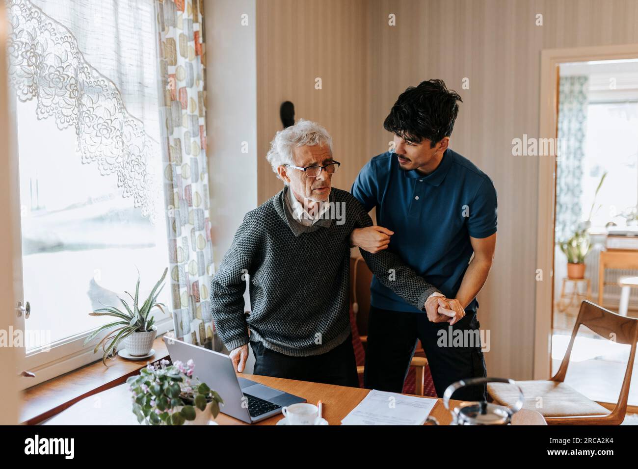 L'operatore sanitario maschile aiuta l'anziano mentre si alza a casa Foto Stock