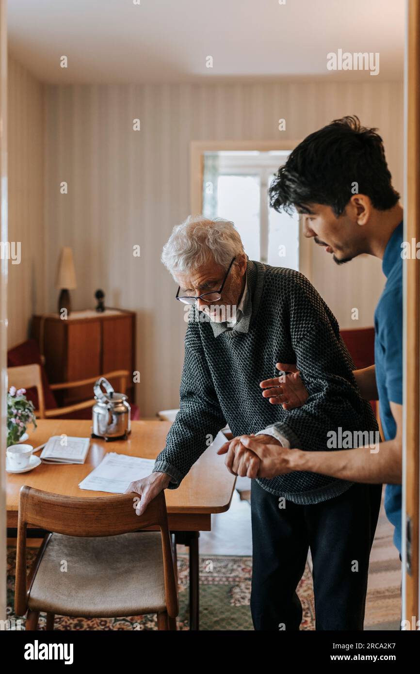 Assistente di cura maschile che aiuta l'anziano a camminare a casa Foto Stock