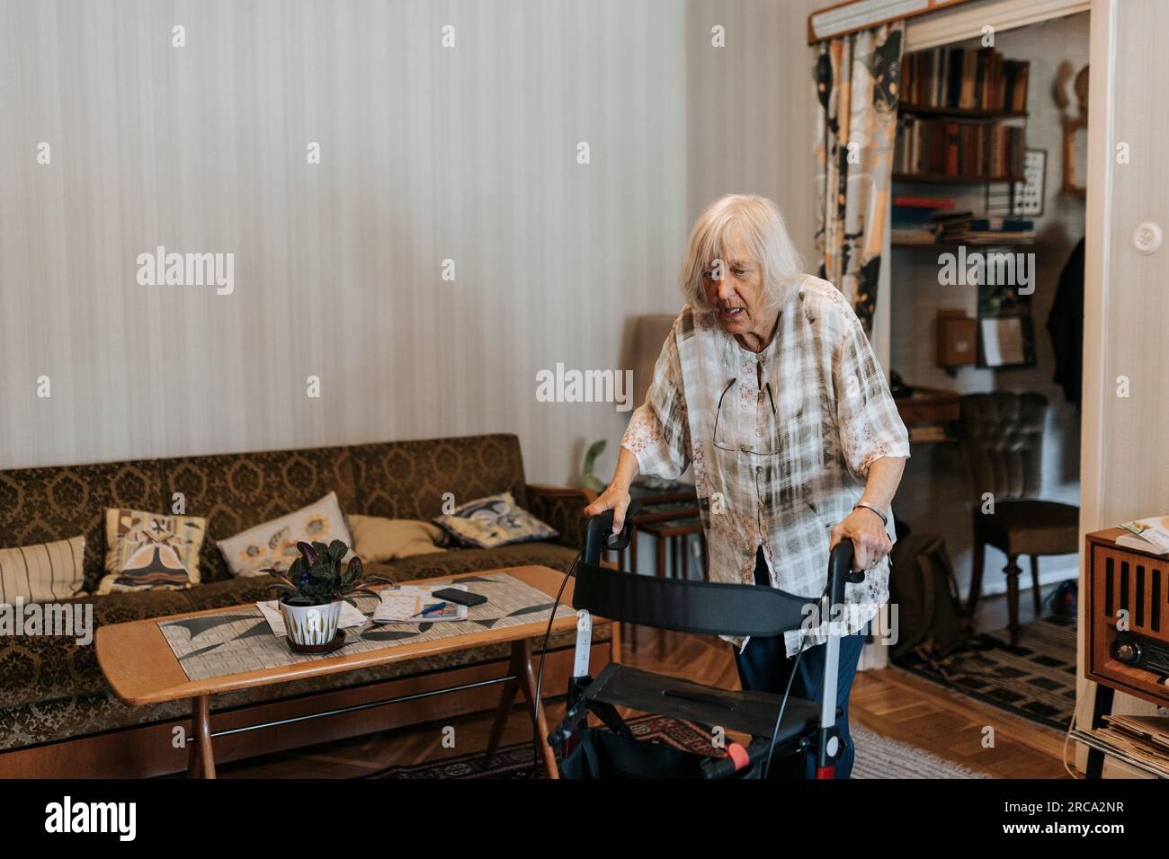 Donna anziana che utilizza un camminatore mobile mentre cammina a casa Foto Stock