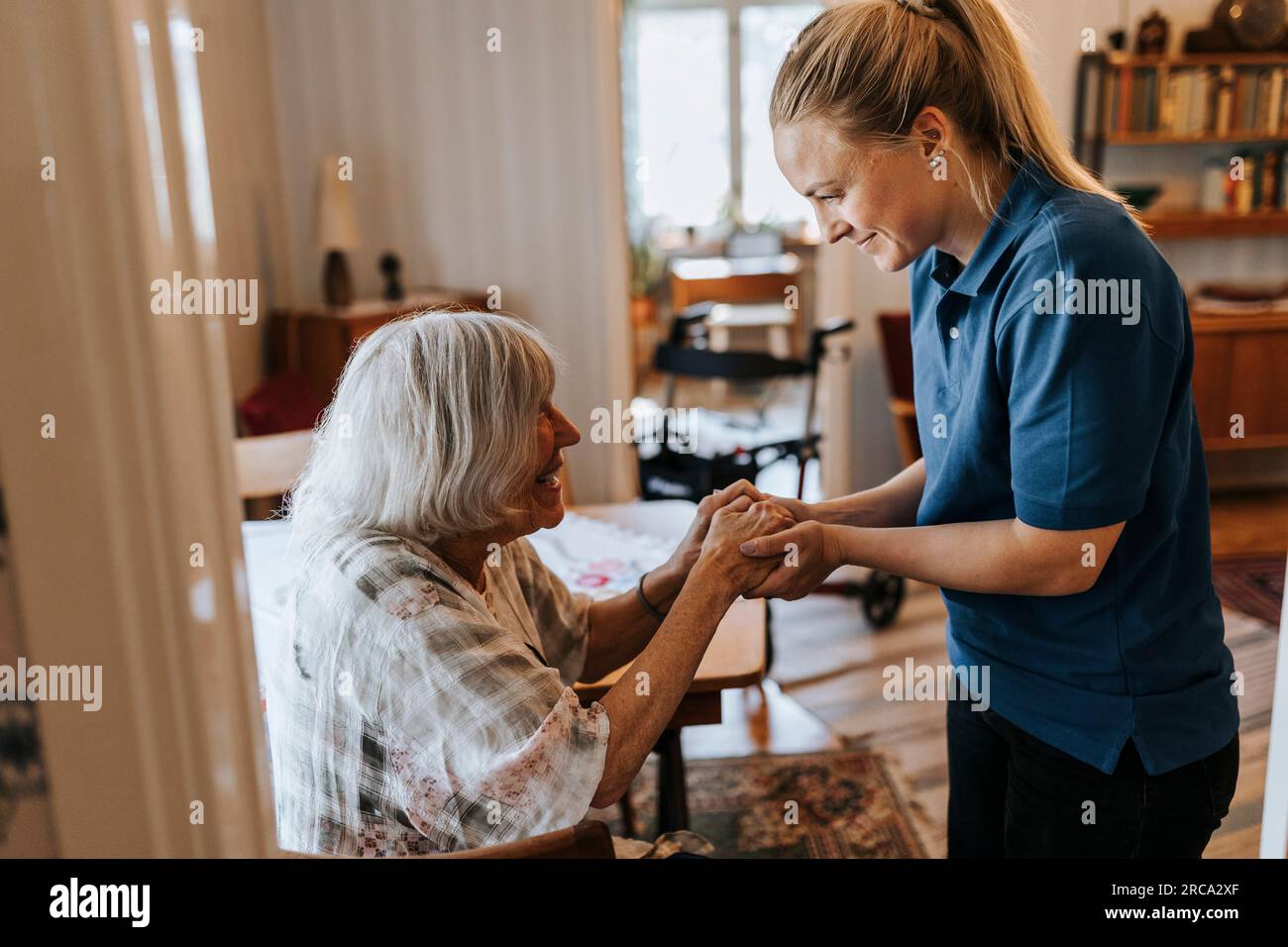 Lavoratrice sanitaria sorridente che tiene per mano di donna anziana a casa Foto Stock