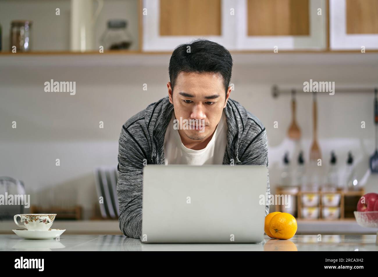 giovane uomo d'affari asiatico che lavora in cucina a casa usando un computer portatile Foto Stock