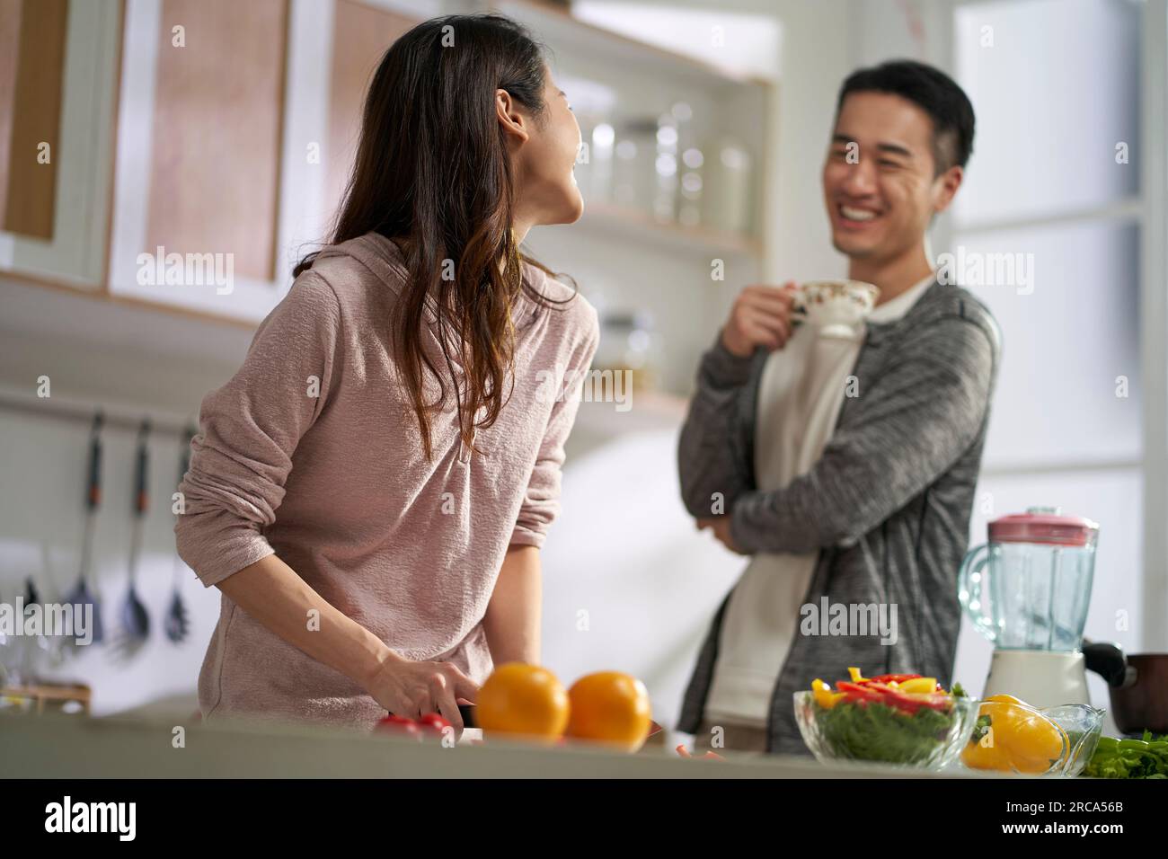 una giovane coppia asiatica felice e amorevole che chiacchiera mentre preparava il pasto insieme in cucina a casa Foto Stock