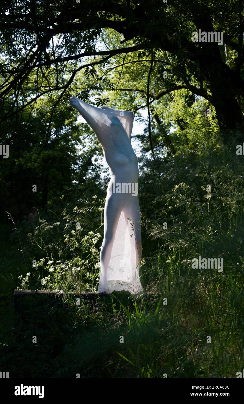 donna nuda sexy con abito a calza in cotone trasparente bianco come scultura moderna all'aperto, retroilluminazione verde del parco naturale, spazio per fotocopie Foto Stock