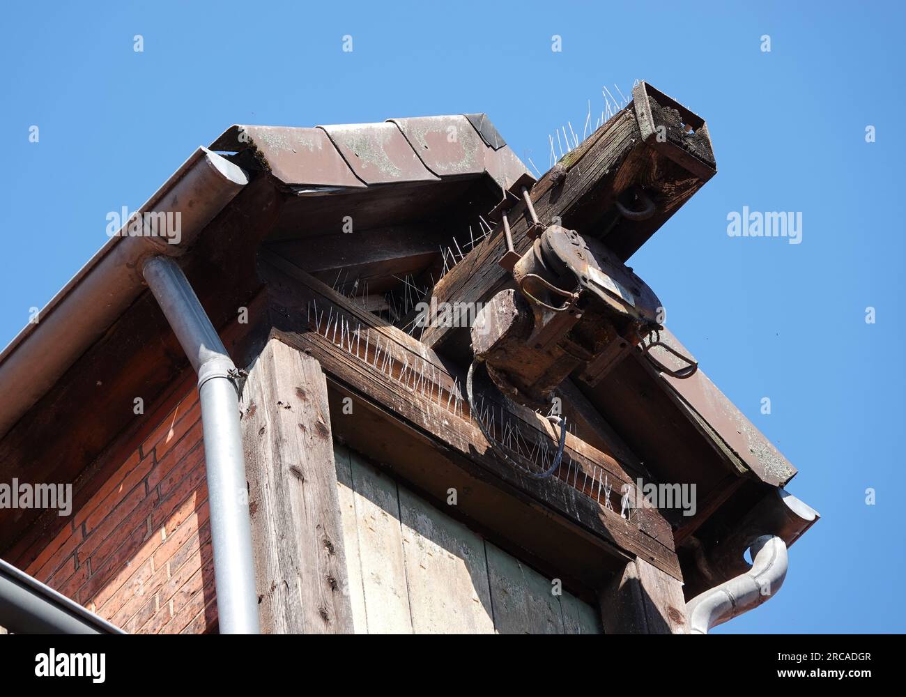 La cresta di un'antica casa con una puleggia per sollevare le cose. Tutto è fissato contro i piccioni con perni. Foto Stock