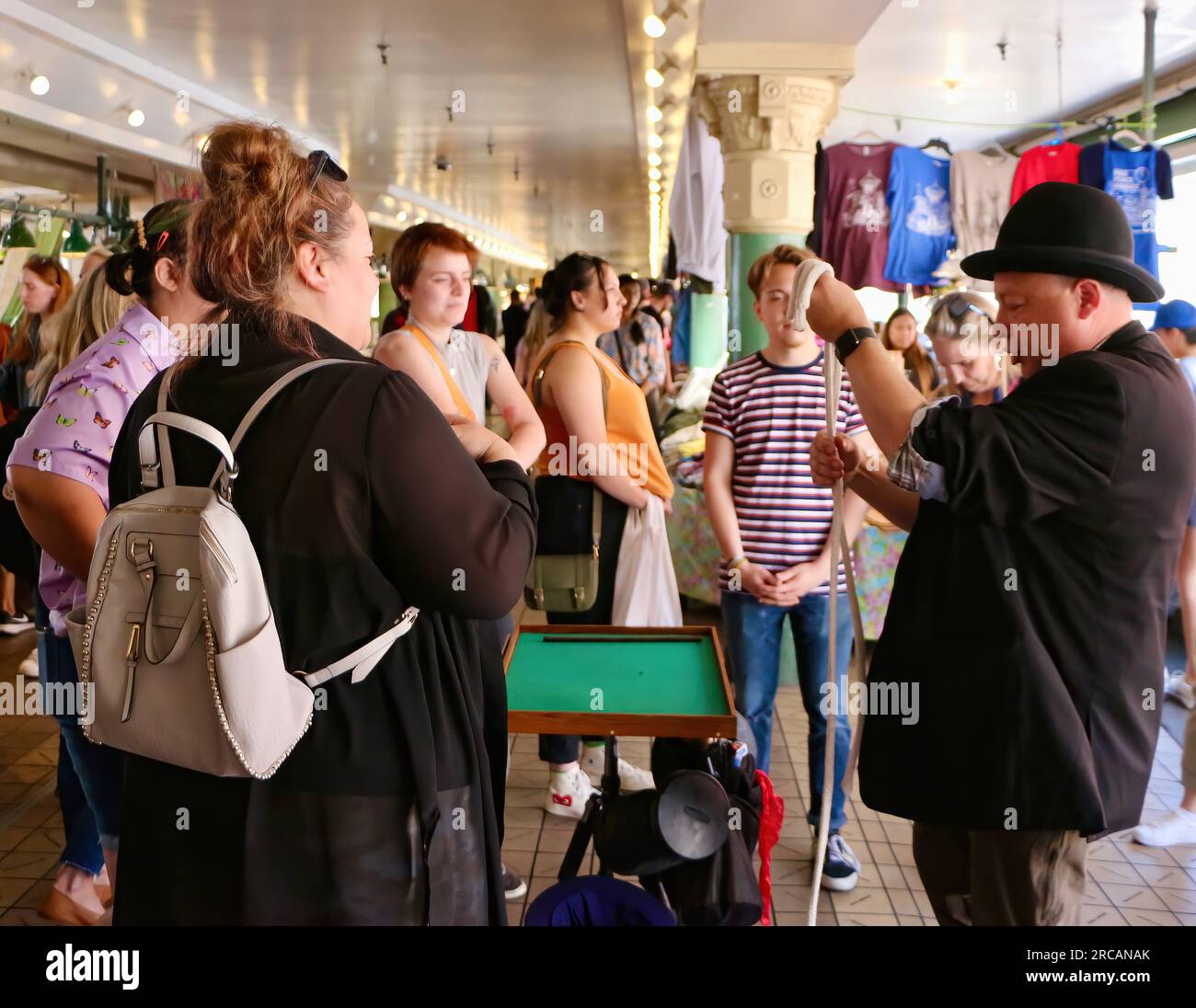 Un mago che si esibisce con un trick di corda indossando un cappello da bowling al Pike Place Market con gente che guarda Seattle, Washington State USA Foto Stock