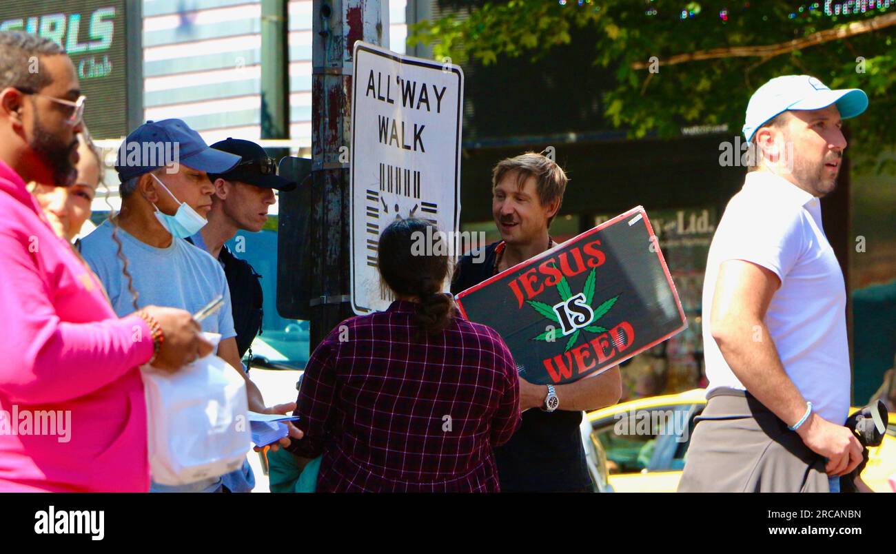 Un uomo con un cartello con una foglia di marijuana che indica Jesus Is Weed all'angolo tra First e Pike con turisti di passaggio Seattle Washington State USA Foto Stock