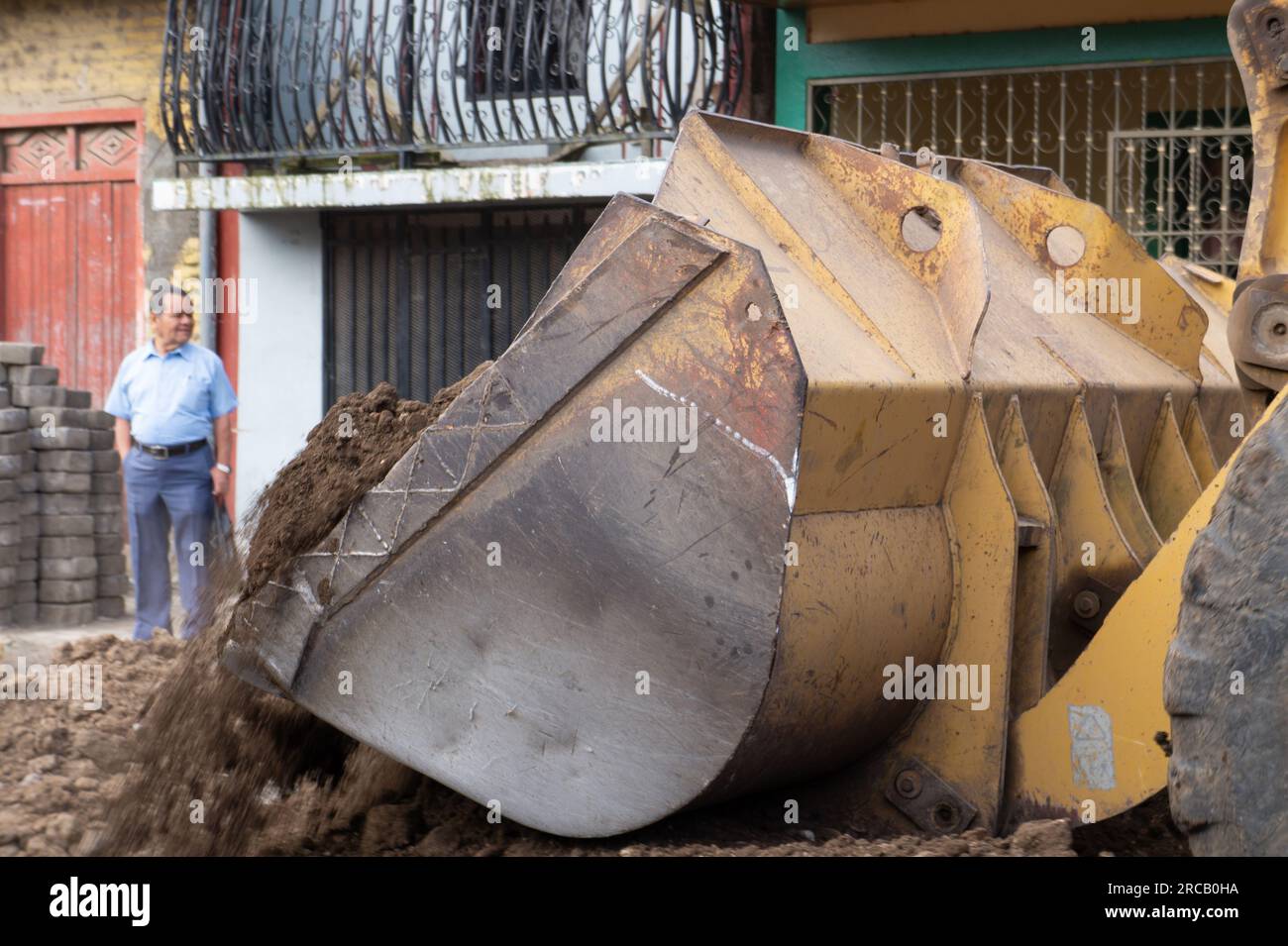 Benna anteriore di una macchina per movimento terra che scarica in anticipo quando l'uomo guarda di lato. Questo faceva parte di una riparazione del sistema fognario a Jinotega, in Nicaragua. Foto Stock