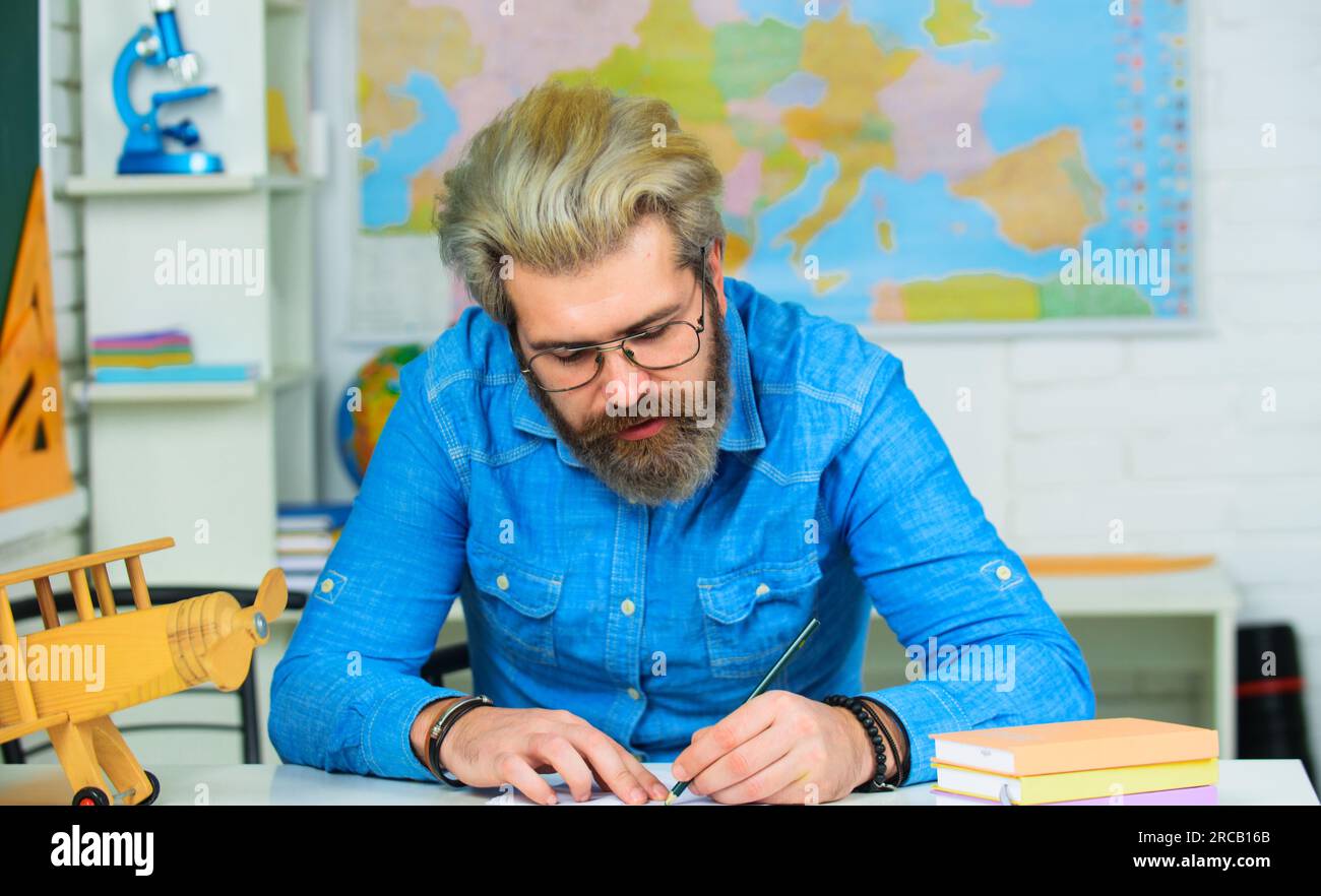 Studente maschio che si prepara per l'esame. Insegnante che lavora al tavolo in classe. Test di conoscenza. Alle superiori. Studente maschio seduto alla scrivania in classe Foto Stock