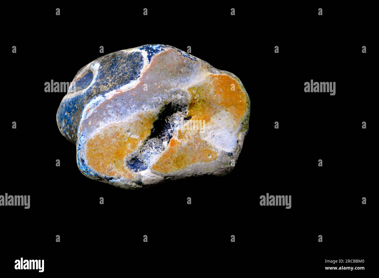 Sezione ravvicinata di una pietra trovata sulla riva del mare e adagiata su uno sfondo nero. Strati di colori vivaci. Foto Stock
