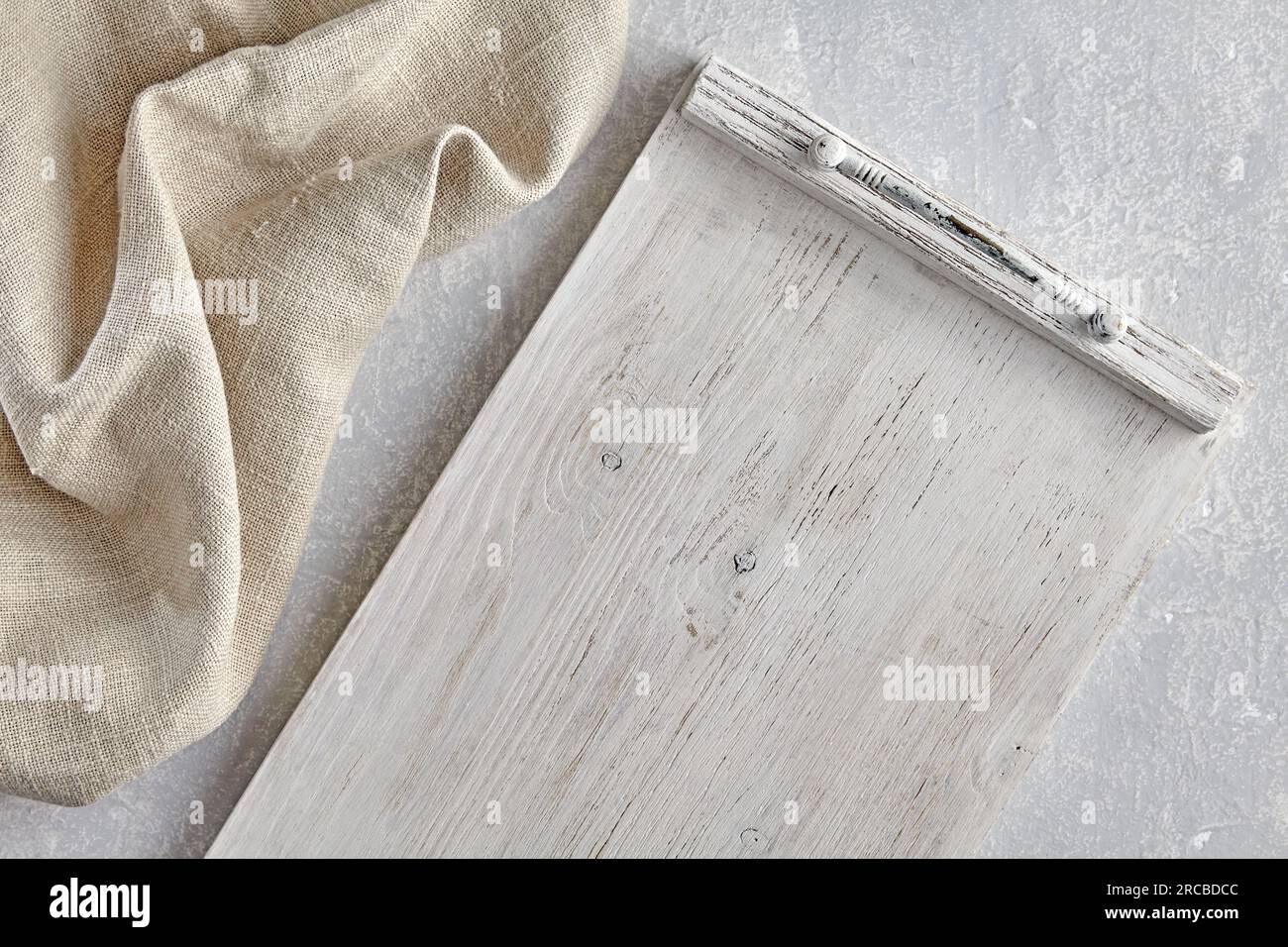 Vassoio in legno dipinto di bianco e tovagliolo da cucina in lino grezzo su un tavolo in pietra chiara. Vista superiore con spazio di copia. Foto Stock