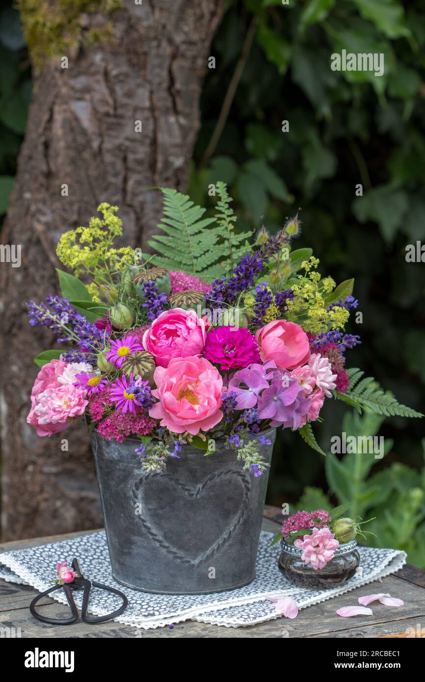 bouquet di rose rosa e fiori estivi in vaso di zinco con ornamenti a cuore Foto Stock