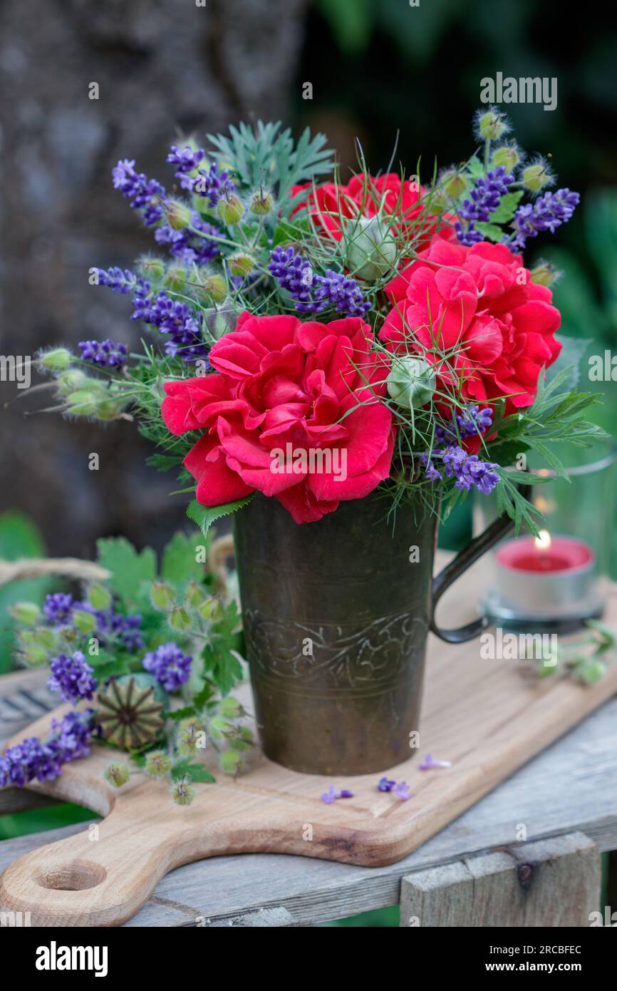 bouquet di rose rosse e fiori di lavanda in una vecchia tazza di rame in giardino Foto Stock