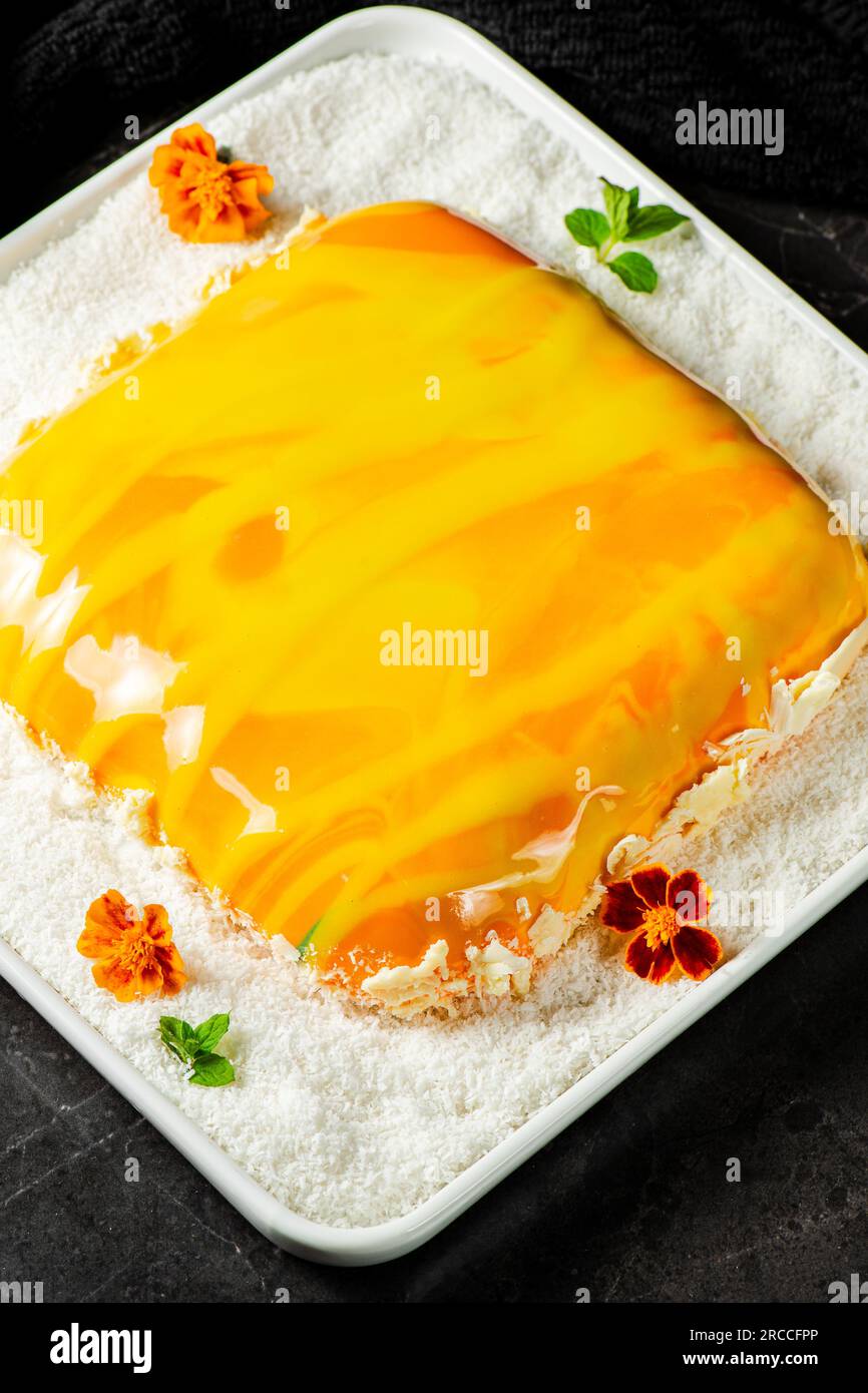 Torta Entremet gourmet con torta spugna stratificata, gelatina di mango, gelatina di crema di cocco e mousse di vaniglia, ricoperta da uno specchio colorato tropicale. Foto Stock