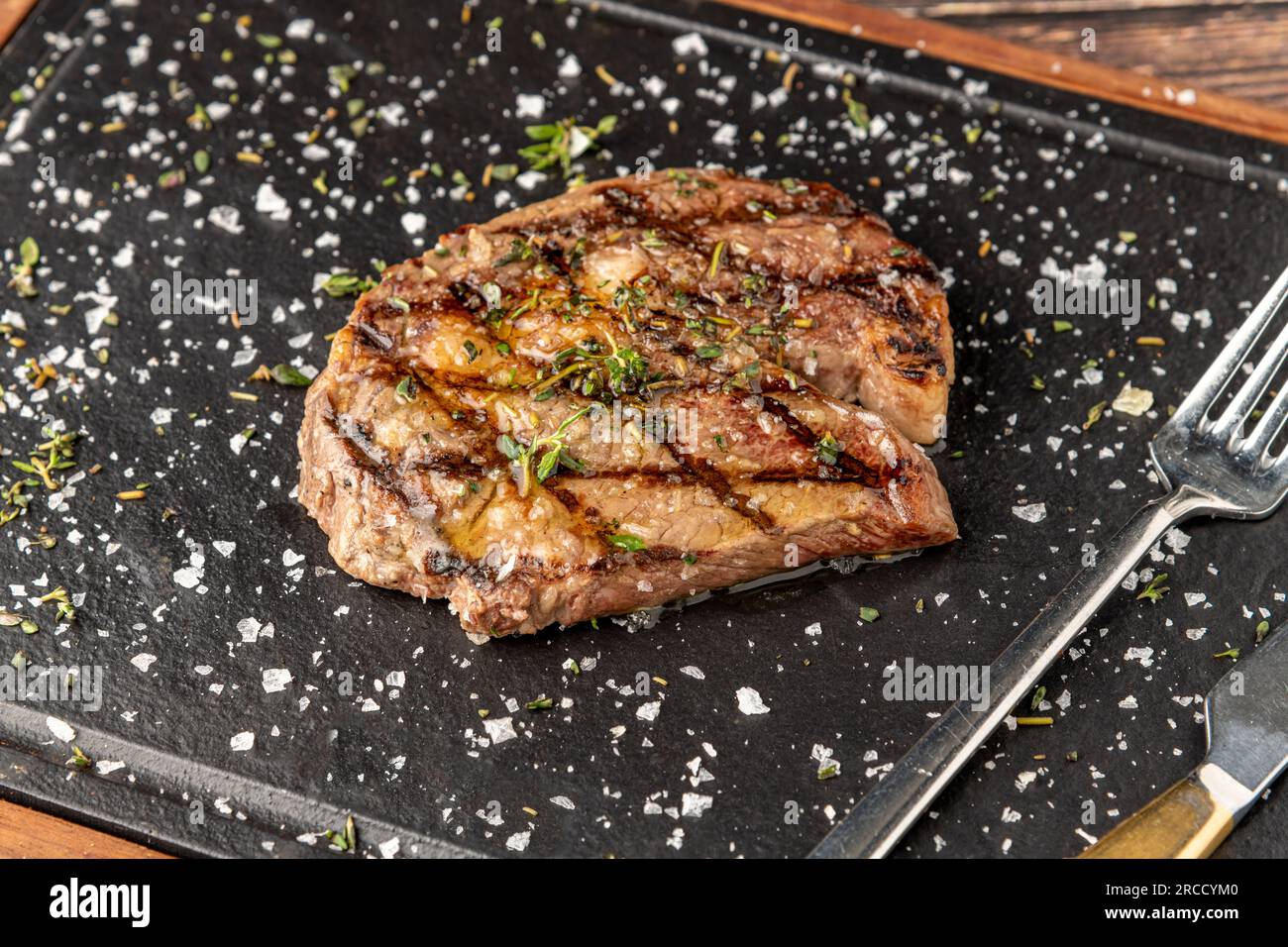 Bistecca di ribeye alla griglia con rosmarino e timo su tagliere di pietra Foto Stock