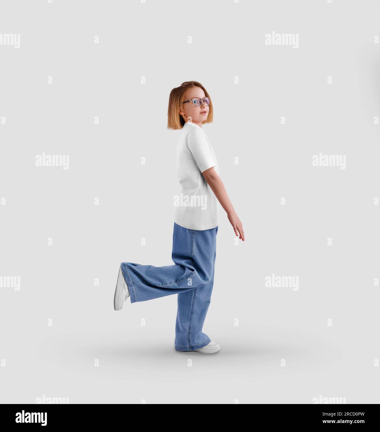 Modello di una t-shirt bianca su un bambino in posa, una ragazza in camicia, jeans, vista laterale, isolata sullo sfondo. Modello di abbigliamento per bambini elegante per des Foto Stock