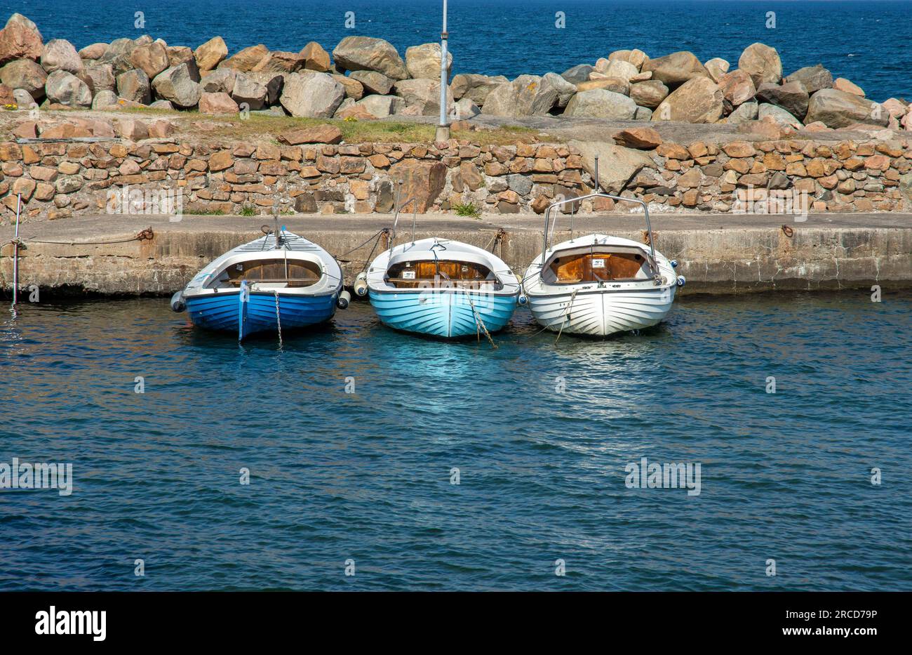 Tre barche a baia con molo di pietra nel sud della Svezia Foto Stock