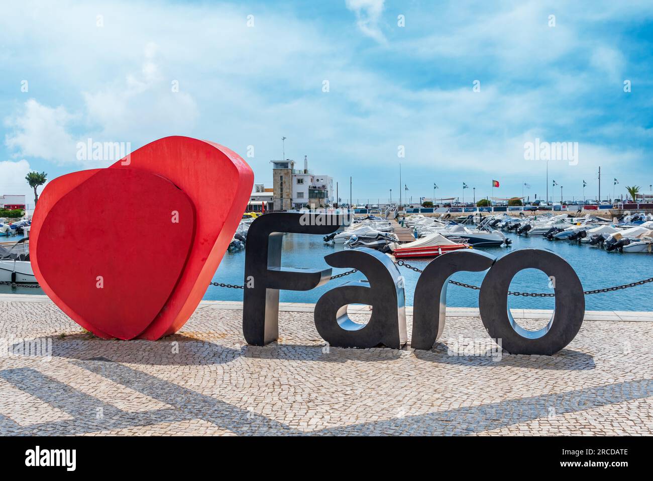 Il nome di Faro accanto ad un grande cuore, un luogo tipico per le foto turistiche, con il porto turistico alle spalle, Algarve. Foto Stock