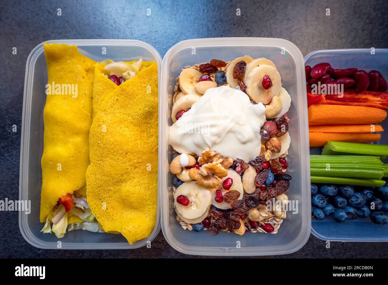 Scatole con cibo sano pieno di verdure e frutta colorate. Noci, mirtilli, yogurt, melograni, banane, frittelle dolci senza glutine, uva passa, celer Foto Stock